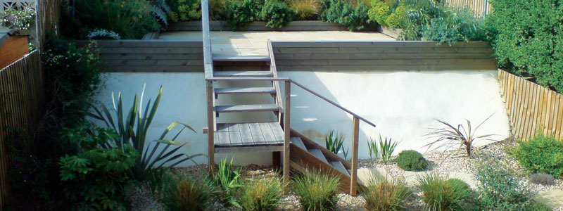 Raised back area of tropical style garden with wooden stair case and stone chip bedding